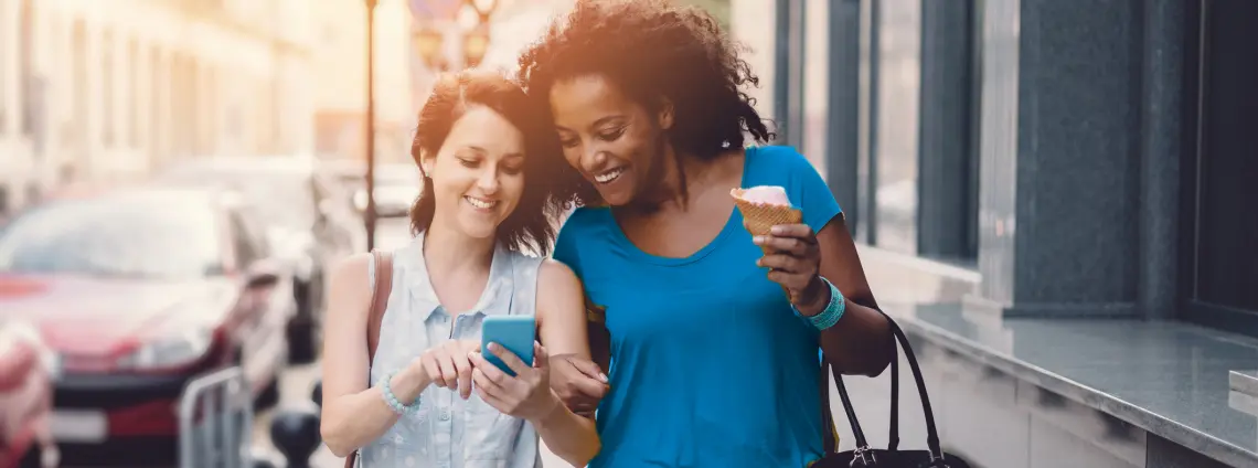 Zwei Frauen laufen auf einer Staße und schauen gemeinsam auf ein Handy