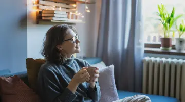 Eine Frau mit Tasse in der Hand sitzt auf ihre Sofa und lächelt