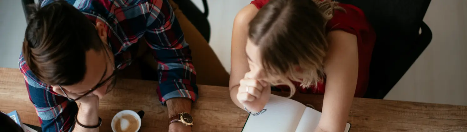 Eine Frau und ein Mann sitzen an einem Tisch und beugen sich über einen Laptop und Papiere