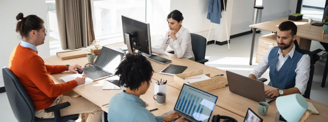 Büro mit vier Personen die vor PCs sitzen und arbeiten