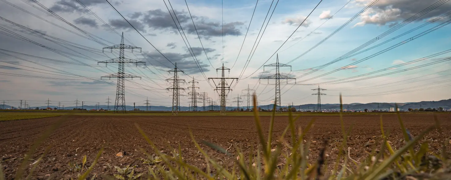 Industriestrom: Hochspannungsleitungen an Strommasten auf einem grünem Feld bei Sonnenuntergang.