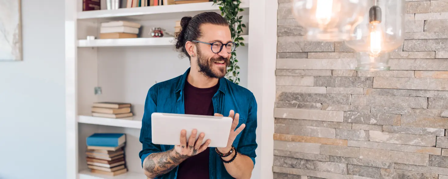 Ein Mann steht mit einem Tablet in der Hand in seiner Wohnung und lacht