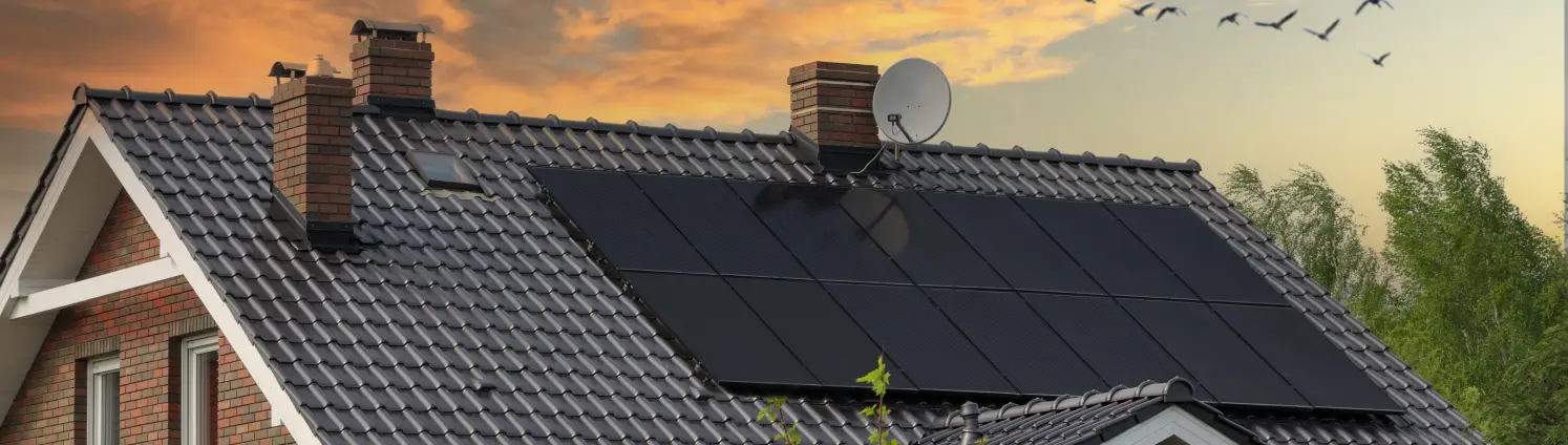 Einfamilienhaus mit Photovoltaikanlage vor rötlichem Abendhimmel.