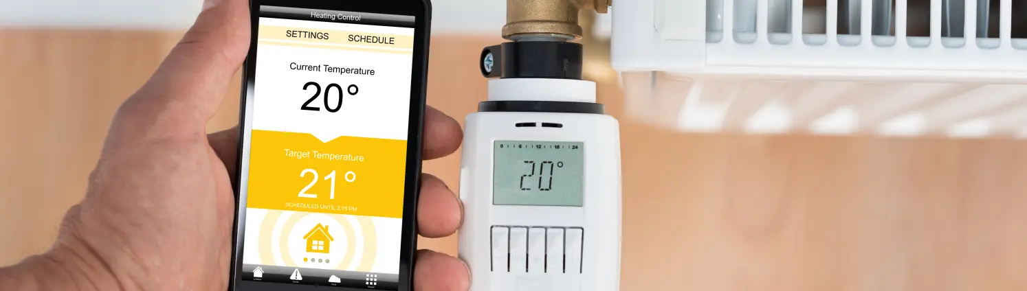 Nahaufnahme der Hand der Person, die die Temperatur des Thermostats mit dem Handy einstellt.