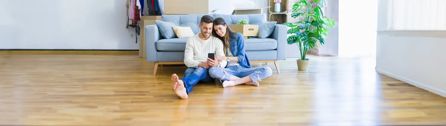 Pärchen sitzt vor einem Sofa auf dem Boden und schaut auf ihr Telefon