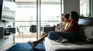 Eine Familie schaut fernsehen und isst dabei Popcorn auf dem Sofa