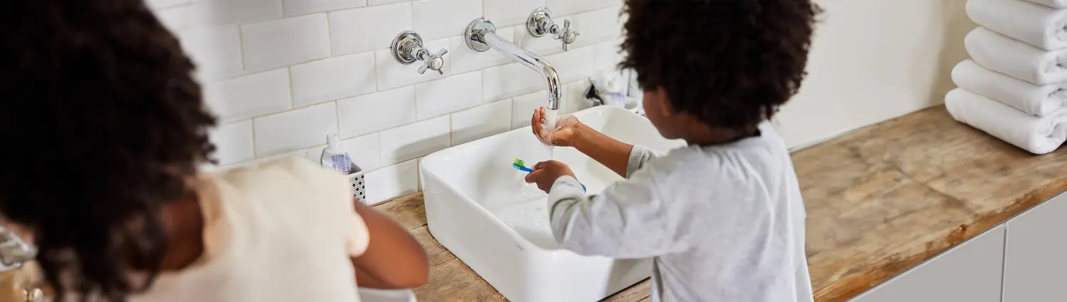 Ein Kind steht an einem Wasserhahn und hält die Hand unters Wasser