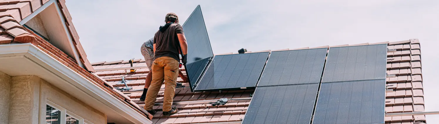 männliche junge Handwerker, die Sonnenkollektoren an Dachhalterungen auf einem Vorstadthaus mit Tonziegeln installieren