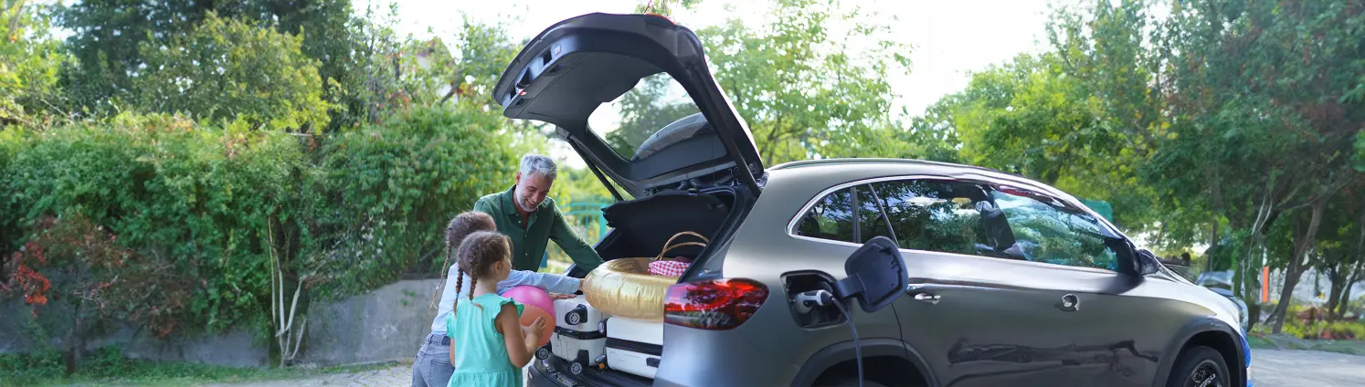 Ein Vater packt mit zwei Töchtern das E-Auto für den Urlaub.