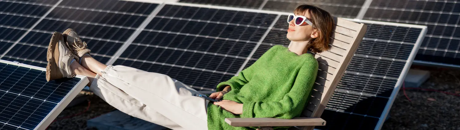 Frau in einem grünen Pullover auf dem Dach ihres Hauses mit einer Solarstation