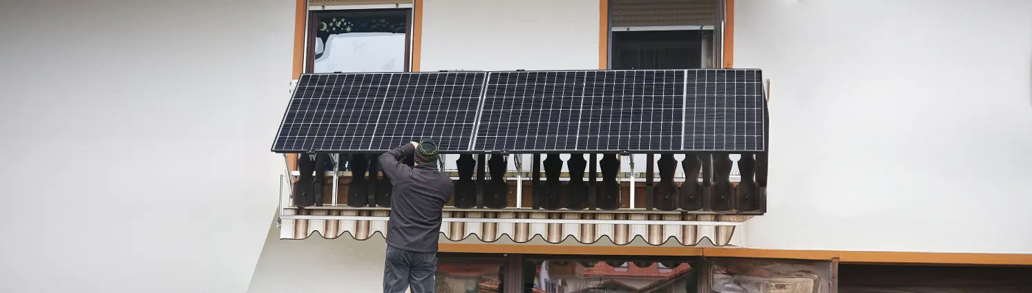 Ein Mann installiert eine Photovoltaik Anlage auf einem Balkon