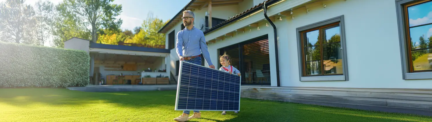 Vater und Tochter tragen ein Solarmodul vor dem Haus