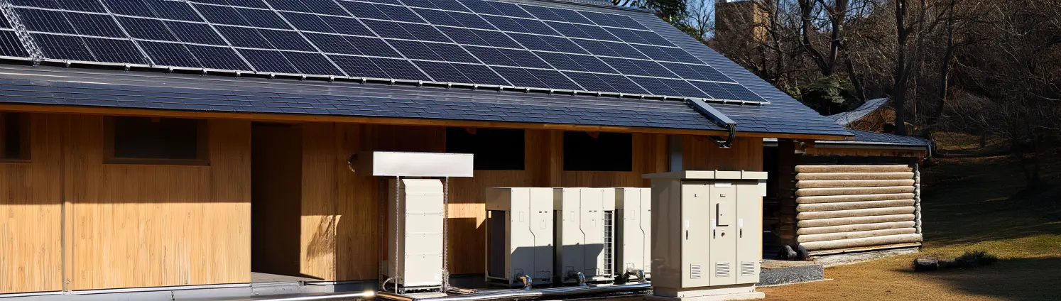 Satteldach mit Photovoltaik-Paneelen und darunter aufgereihten Stromspeicherkästen.