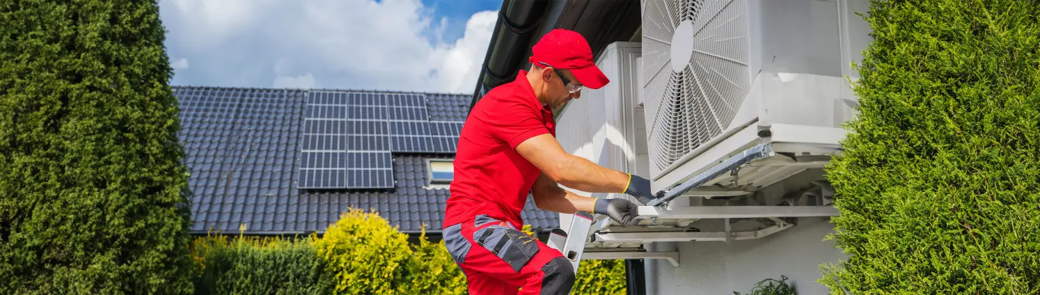 Techniker wartet eine an der Hauswand montierte Wärmepumpe.