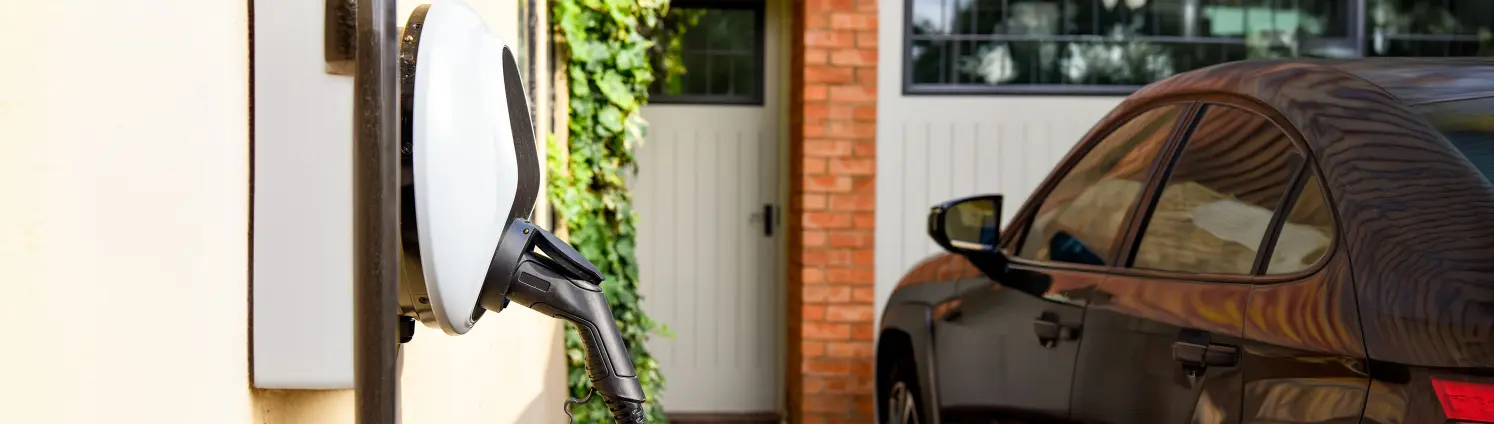 An der Wand installierte Wallbox mit Auto vor Garage