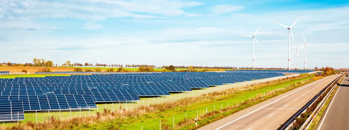 Auf einem Feld neben einer Straße ist eine Photovoltaik-Anlage und Windkrafträder zu sehen