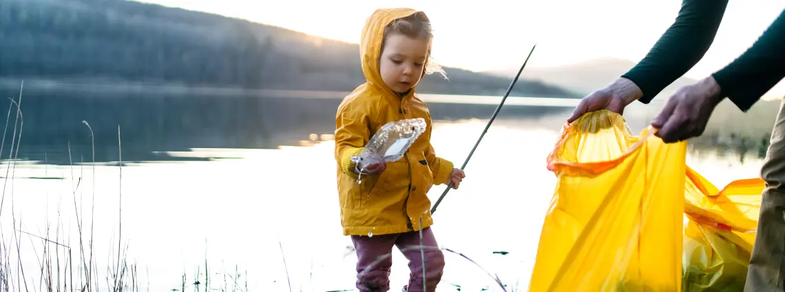 Ein Kind sammelt mit dem Vater Müll an einem Fluss ein