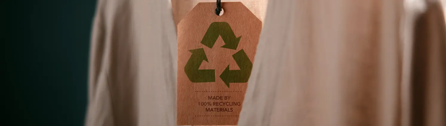 Auf einem Kleiderbügel hängt ein Cardigan und ein Etikett mit dem Recycling-Logo hängt herunter