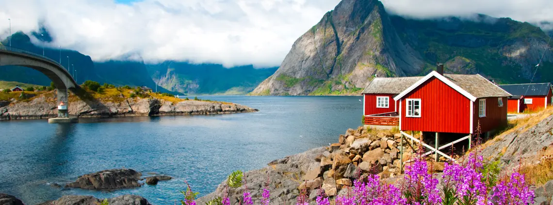 Ein rotes Holzhaus steht am Rand eines Fjords