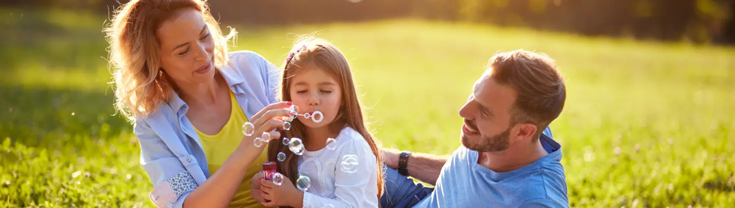 Mutter, Vater und Tochter sitzen im Frühling im Park und pusten Seifenblasen